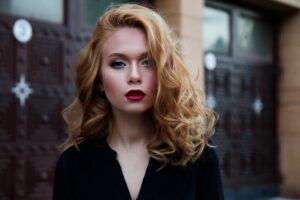 Elegant portrait of a woman in a black top with striking red lips and flowing blond hair.