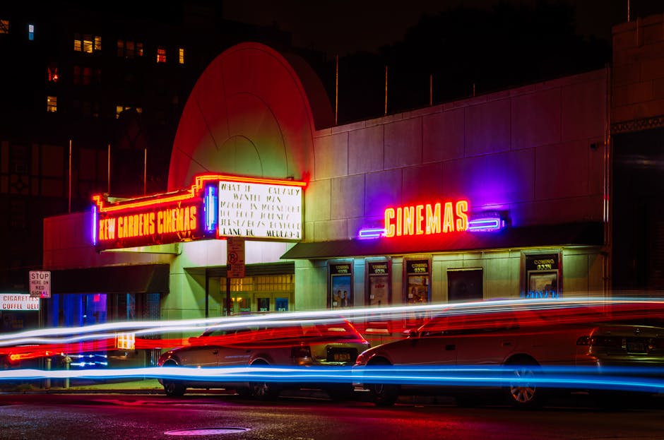 Vibrant night view of New Gardens Cinemas in Queens, New York with colorful neon lights and light streaks.